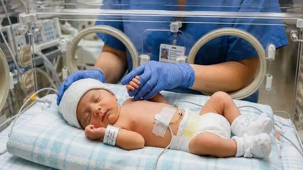 infant in nicu holding hands with nurse